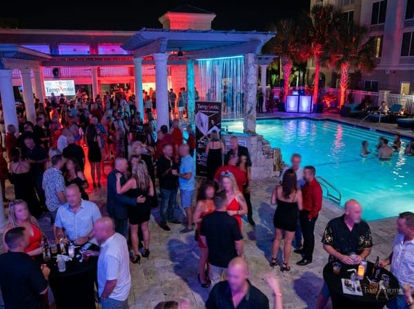 Guests filling the pool deck and pergola bar at a TampArotic hotel-takeover pool party in Tampa Bay — faces blurred for privacy.