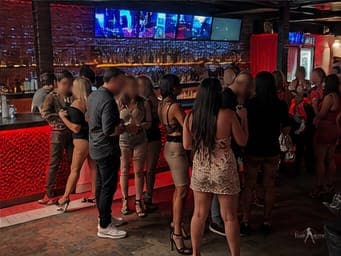 Guests gathered at the back bar under the screens at a TampArotic lifestyle night — faces blurred for privacy.