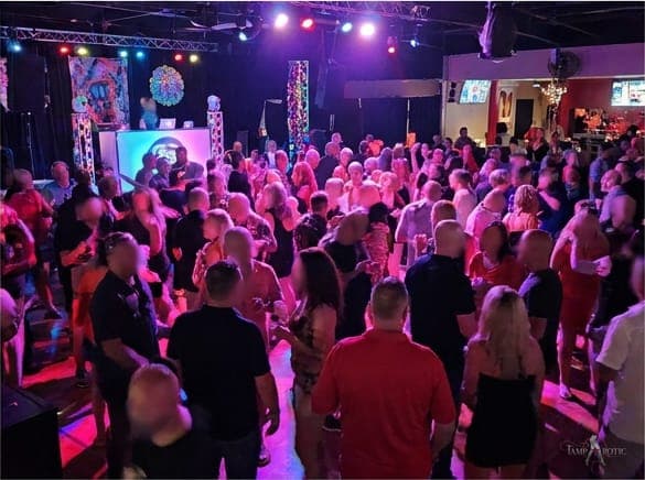 A full dance floor from behind, washed in magenta light at a TampArotic lifestyle party in Tampa Bay.