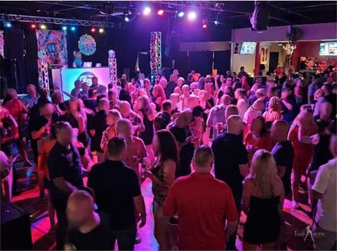 A full dance floor washed in magenta light at a TampArotic lifestyle party — faces blurred for privacy.
