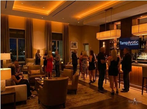 Guests mingling in the warm hotel lounge and bar at a TampArotic Tampa Bay event — faces blurred for privacy.