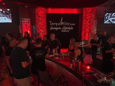 An earlier TampArotic night in the red-lit columned lounge, under the original event banner — faces blurred for privacy.