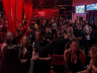 Guests in the red-lit lounge at a TampArotic lifestyle event — faces blurred for privacy.