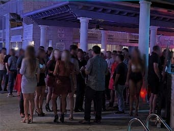 A crowd on the pool deck under violet light at a TampArotic hotel-takeover — faces blurred for privacy.