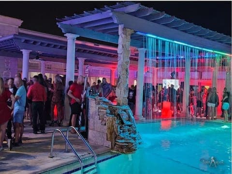 Guests along the pool deck and pergola early in a TampArotic hotel-takeover evening — faces blurred for privacy.