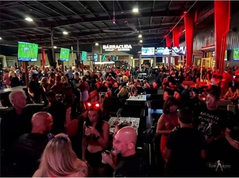 A packed sports-bar takeover crowd mingling under the screens at a TampArotic Tampa Bay night — faces blurred for privacy.